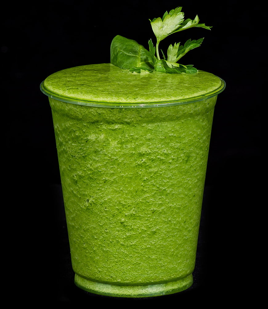 Vibrant green detox smoothie in plastic cup with parsley garnish