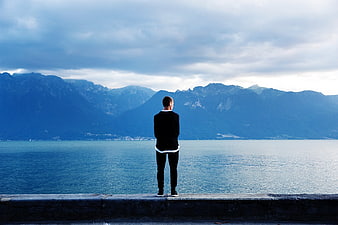 Man standing on pier looking at lake and mountains