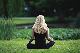Woman meditating in lotus position on grass near a lake