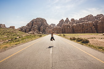 Woman jumping on desert road with rock formations