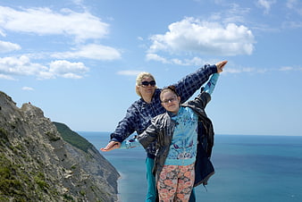 Mother and daughter posing with arms outstretched on coastal cliff