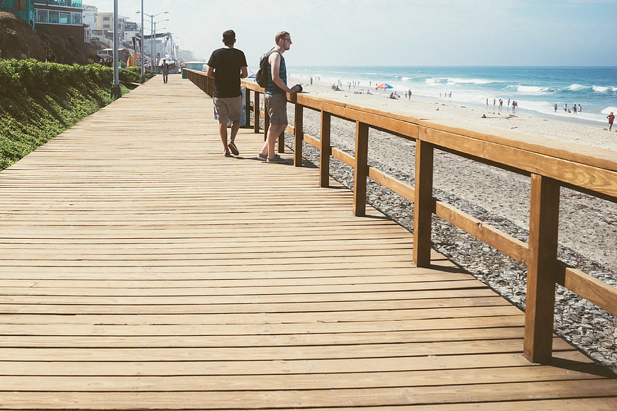 Men walking on wooden boardwalk near sunny beach