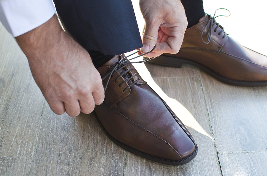 Man tying brown leather dress shoes on wooden floor