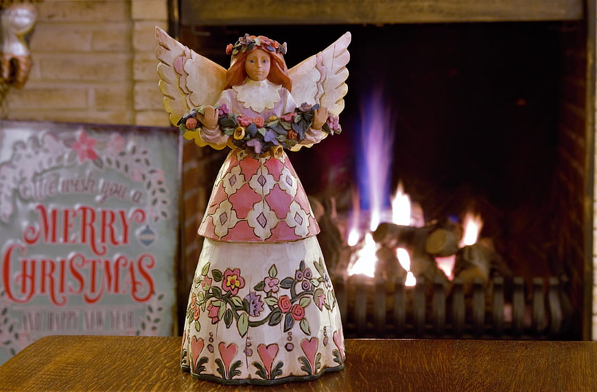 Hand-painted wooden angel figurine by a fireplace
