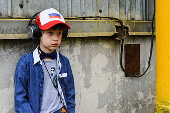 Young boy with headphones and cap standing against distressed concrete wall