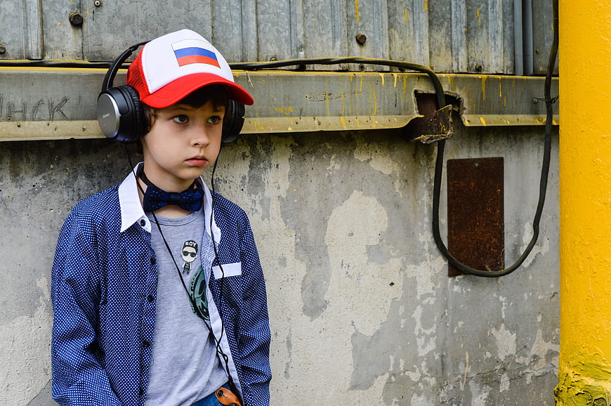 Young boy with headphones and cap standing against distressed concrete wall