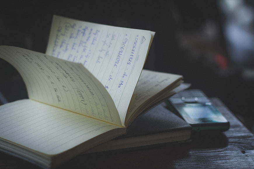 Open Notebook with Handwritten Notes and Smartphone on Desk