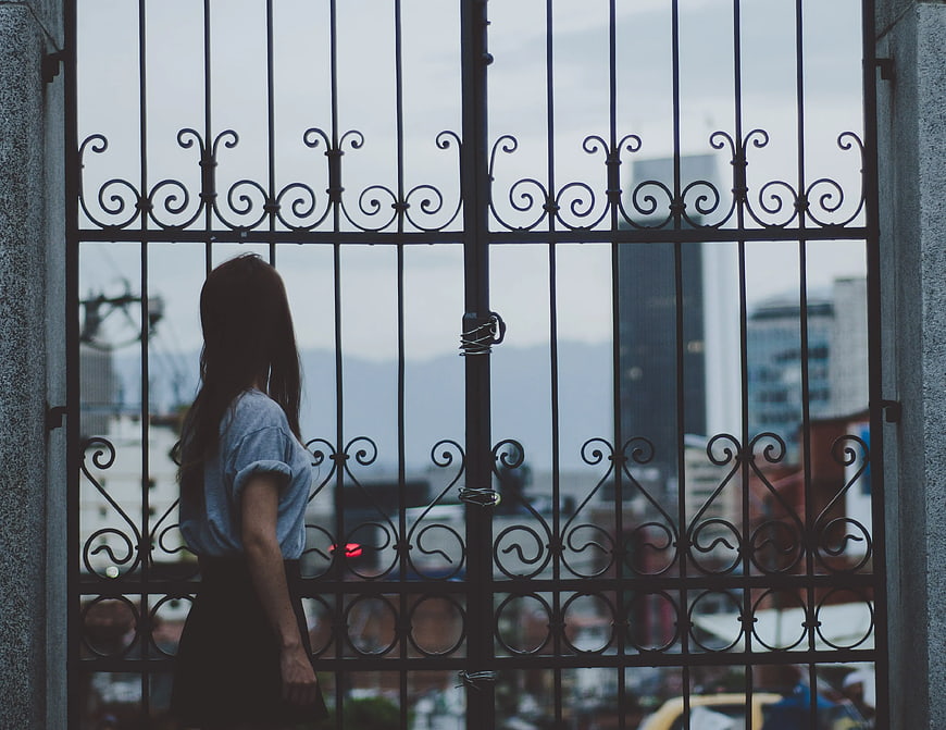 Woman Standing Beside Ornate Metal Gate