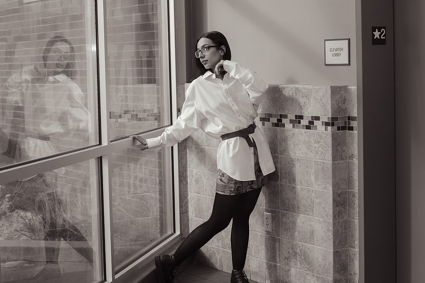 Stylish woman in white shirt posing by window in black and white