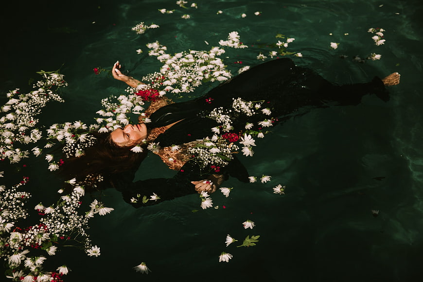 Woman Floating in Dark Water Surrounded by White Flowers