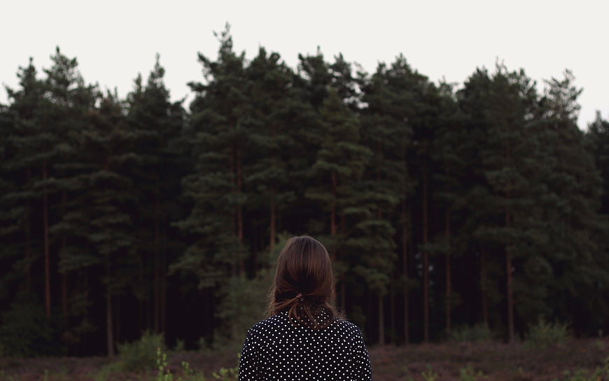 Woman Looking at Dark Pine Forest from Behind