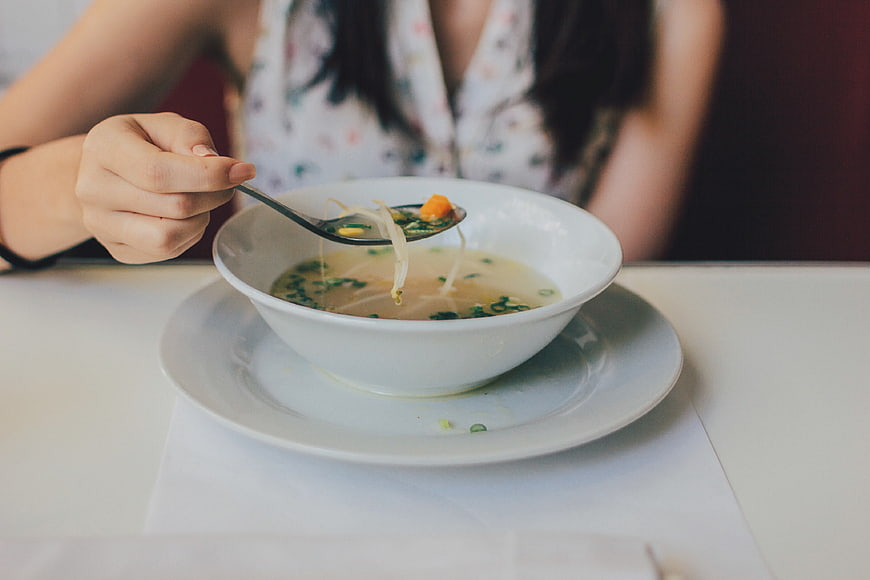 Woman Eating Soup with Spoon in White Bowl