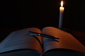 Black Pen on Open Book with Lit Candle