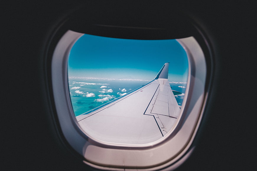 Airplane Wing View Through Window Over Clouds and Ocean