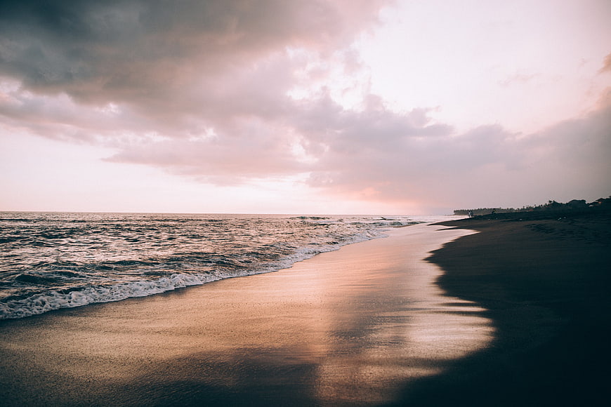 Serene Beach Sunset with Pink Clouds and Wet Sand Reflections