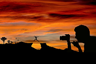 Silhouette of Photographer Capturing Jumping Figure Against Vibrant Sunset Sky