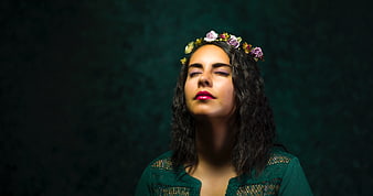 Woman with flower crown meditating against dark green background