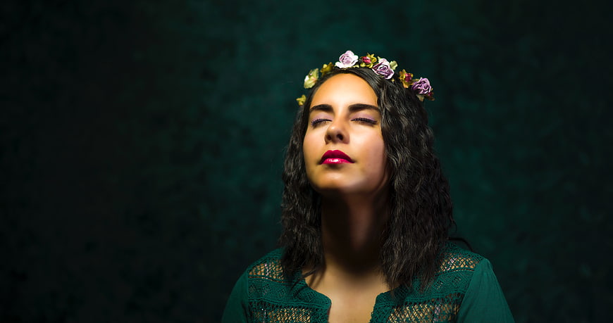 Woman with flower crown meditating against dark green background