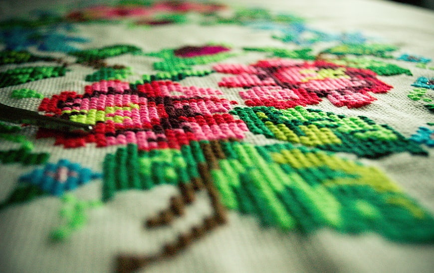 Close-up of colorful floral cross-stitch embroidery on linen fabric