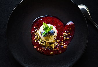 Gourmet dessert with berry sauce and nuts on black plate