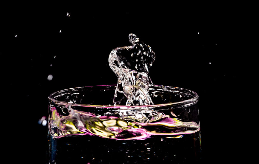 Dynamic water splash in glass with colorful reflections on black background