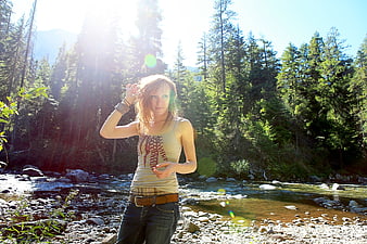 Young woman standing by a sunny forest river stream