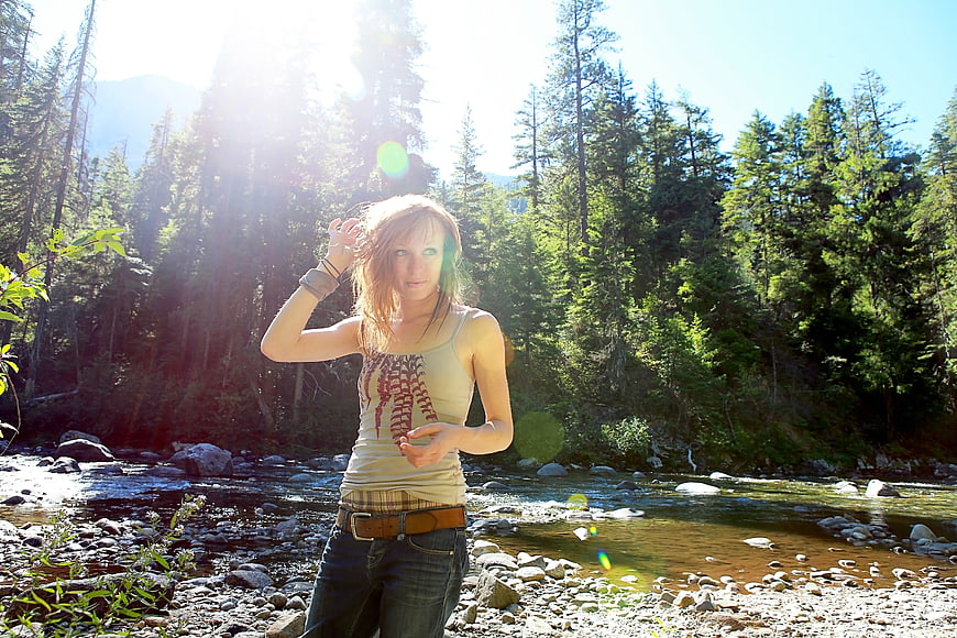 Young woman standing by a sunny forest river stream