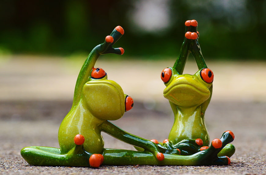 Two green ceramic frogs doing yoga poses outdoors