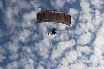 Parachutist descending against a blue sky with scattered clouds