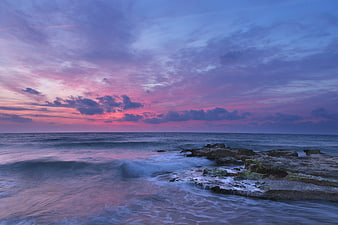 Dramatic purple and pink sunset over rocky ocean coastline