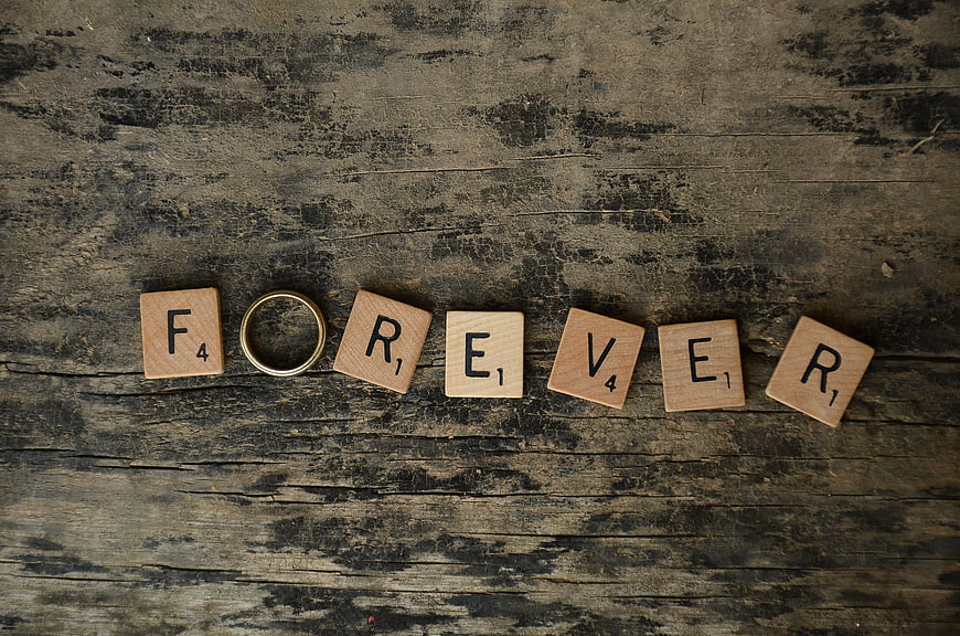 Scrabble tiles spelling forever with wedding ring on wood