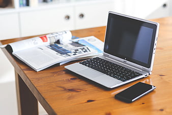 Silver laptop, smartphone, and magazine on wooden desk