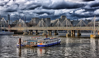 Dramatic cloudy sky over London Millennium Bridge and river boats