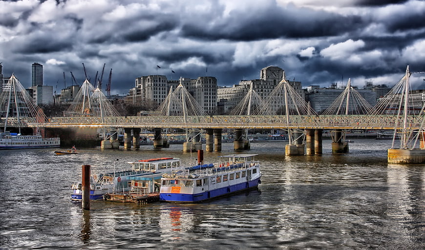 Dramatic cloudy sky over London Millennium Bridge and river boats