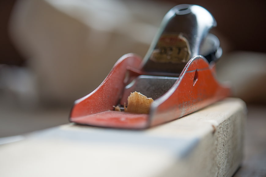 Close-up of red hand plane on wood with shavings