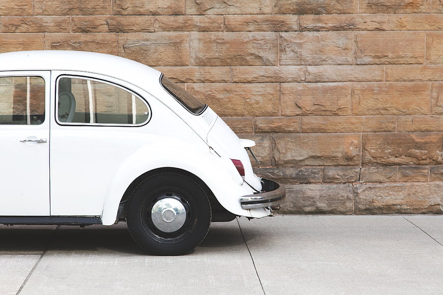 Side view of white vintage Volkswagen Beetle against stone wall