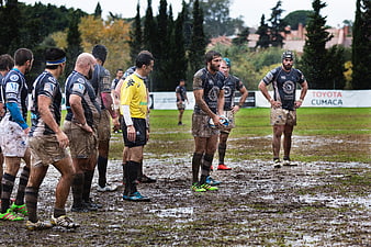 Muddy rugby players standing on wet field during match