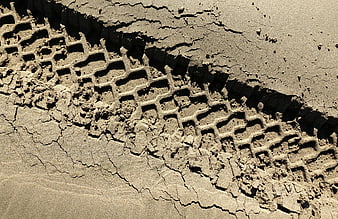 Close-up of vehicle tire tread tracks in cracked dry sand