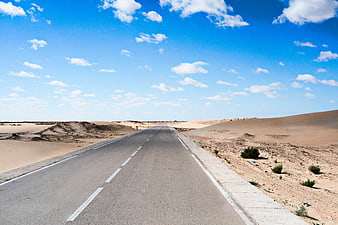 Empty asphalt road stretching through desert landscape under blue sky