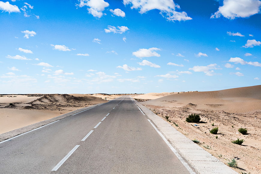 Empty asphalt road stretching through desert landscape under blue sky