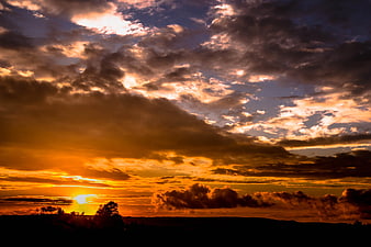 Dramatic sunset with golden clouds over dark silhouette landscape