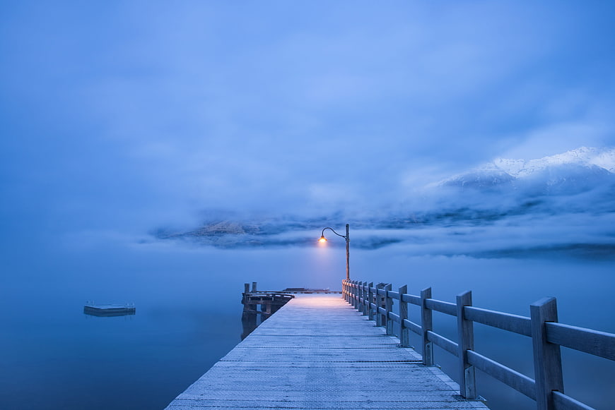 Serene wooden pier extending into misty blue lake at dusk