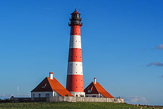 Red and white striped lighthouse on a grassy hill against blue sky