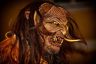 Close-up of a menacing Krampus mask with glowing yellow eyes and sharp teeth