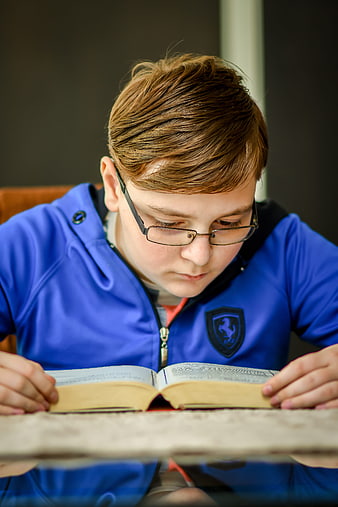 Young boy with glasses reading a book at a table