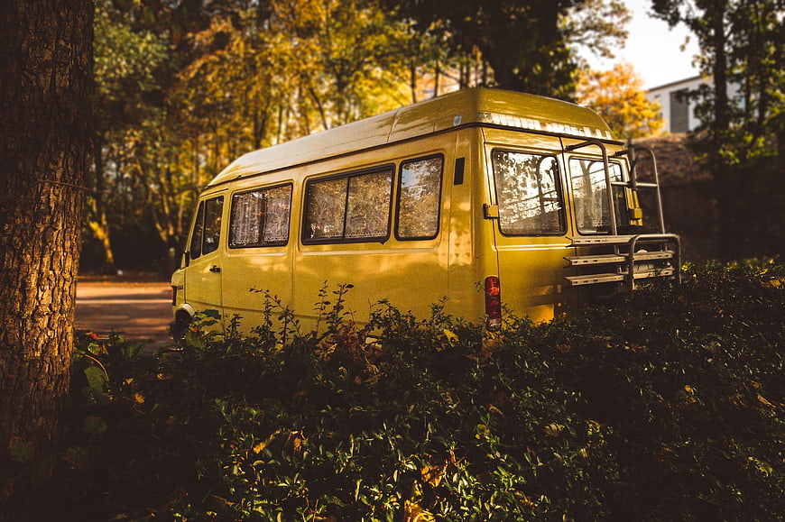 Vintage yellow camper van parked in autumn forest