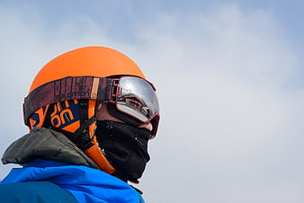 Close-up of skier in orange helmet and goggles against sky