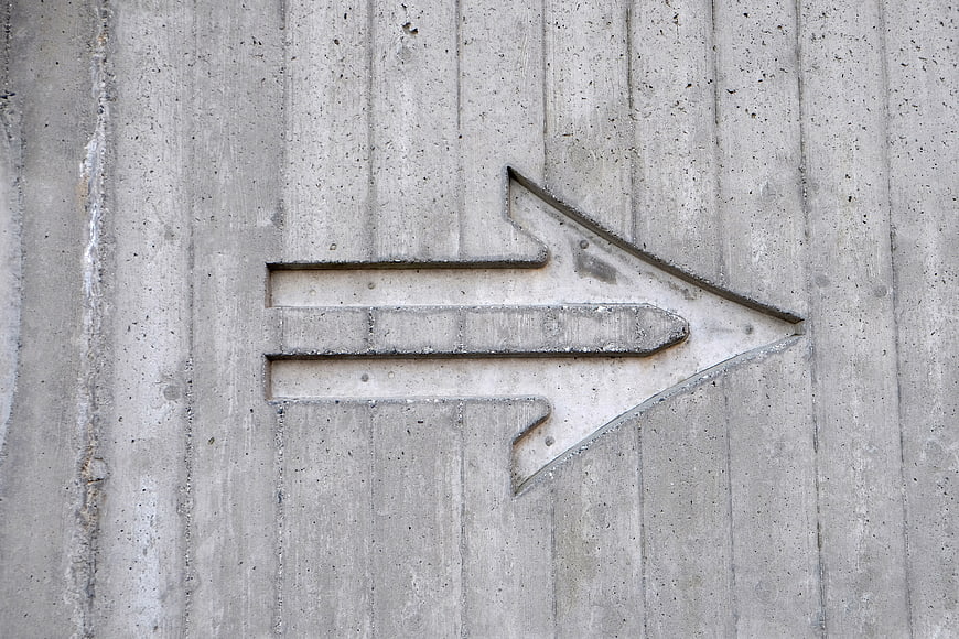 Concrete arrow sign engraved on gray cement wall