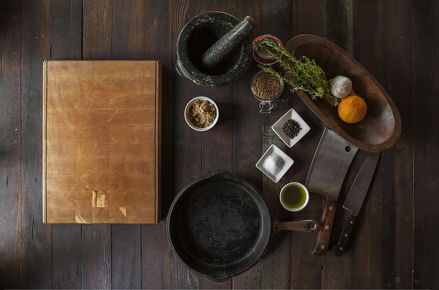 Top view of rustic kitchen tools, spices, and ingredients on dark wood