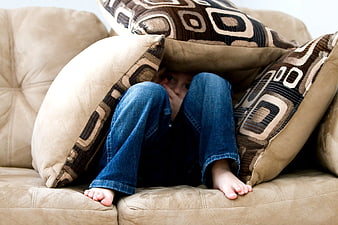Child hiding under pillows on beige sofa